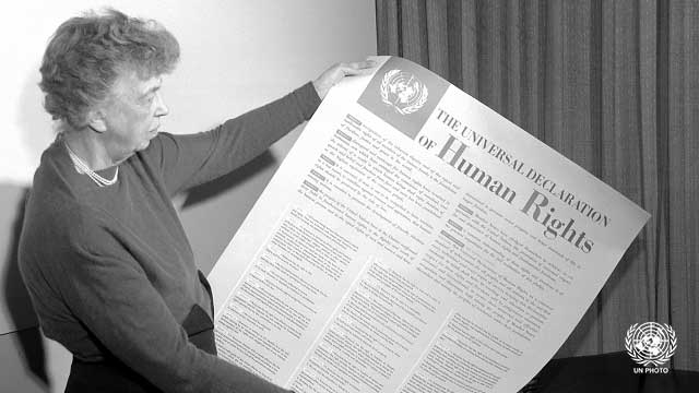 B&W; Woman holds up a huge piece of paper entitled The Universal Declaration of Human Rights.